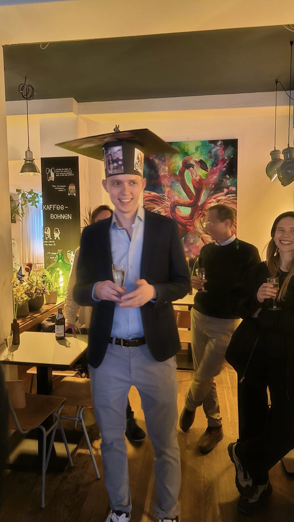 Peter in a decorated doctoral hat, holding a glass of champagne at his PhD graduation celebration.
